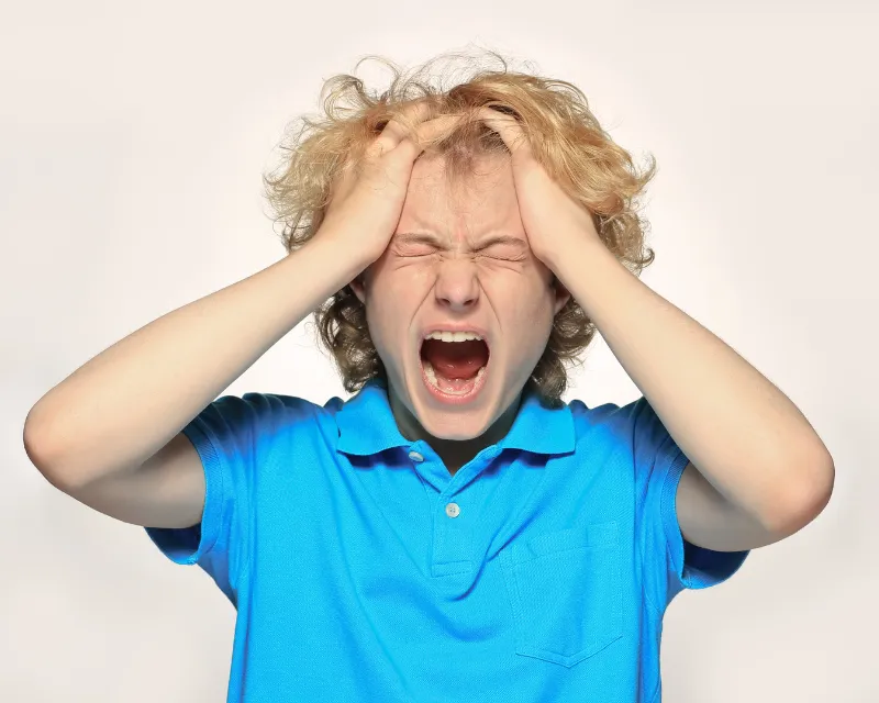 A teenage boy shouting with his eyes closed and his hands on his head showing teenage anger towards mother