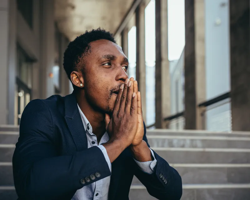 man in a suit sat on some steps outside of his workplace wondering if his anxiety is a disability and what it means for work and everyday life