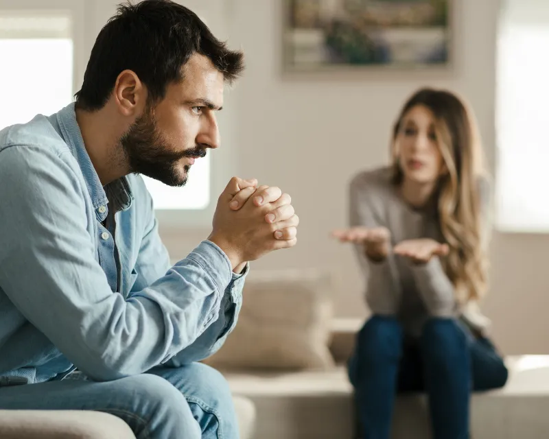 image of a couple sat on adjoining sofas. the man has his hands claspsed together leaning on his knees looking out into the distance and the woman is sat with her hands out palms up wondering. this represents what falling out of love can feel like
