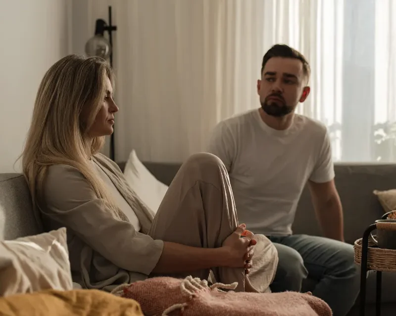 a couple sat in a living room on the sofa after a discussion the representing the experience of PMDD relationship doubts and the uncertainty they bring