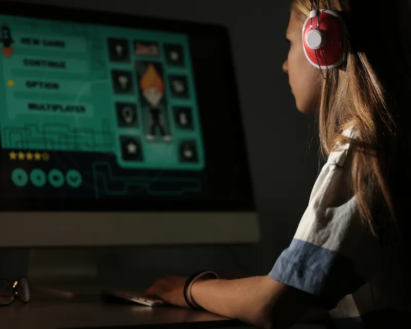 Teenage girl sat at a computer late at night with headphones on playing a game showing how much sleep should teens get