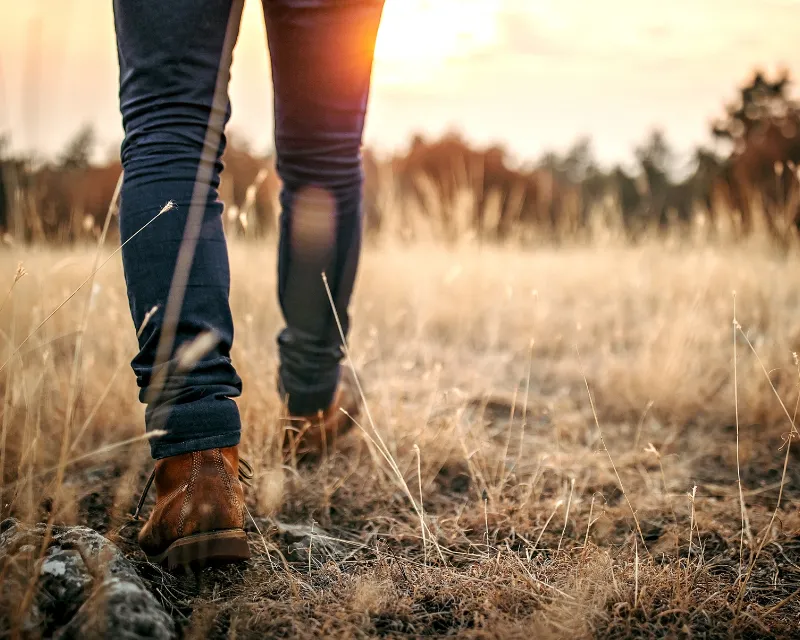 An image of a man's legs wearing jeans and brown walking boots walking through a field at dusk showing what ADHD Burnout Recovery can look like