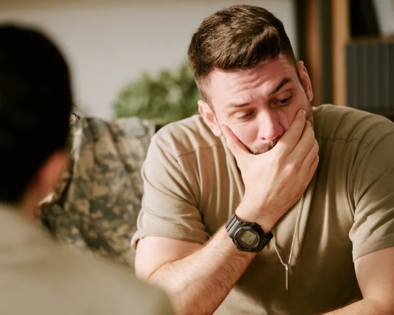 A gentleman sat in a therapists office with his hand covering his mouth looking down at the floor attending bereavement counselling