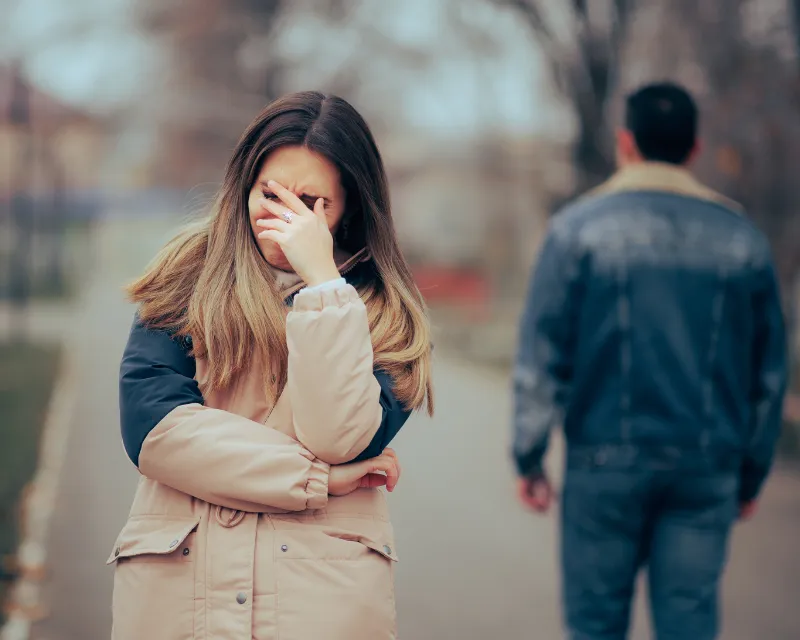 A man walking away from a woman on a winters day outside who has her hand over her face crying showing grief after a breakup